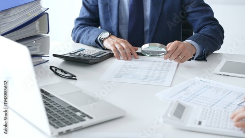 Canvas Print Male financial analysts with female colleague examining documents, using magnifying glass and calculator at workplace in office