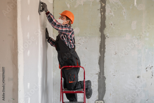 Woman builder or repairman with an emery tool sanding a plastered wall. copy space