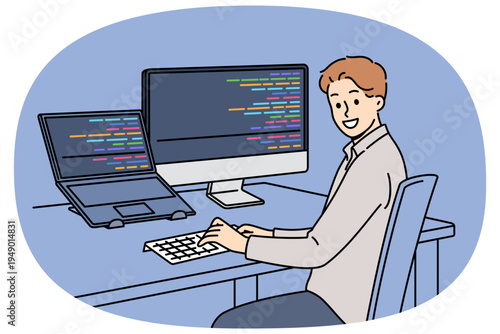 Man programmer types code and looks at camera, sitting at table with computer and laptop. Successful guy programmer develops software or application, working in team with UI or UX designers