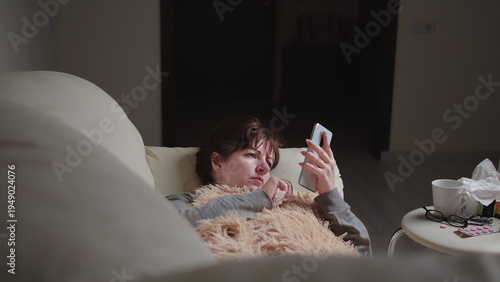 Photography sick brunette woman lies on the sofa and use a phone in the evening, have fun an