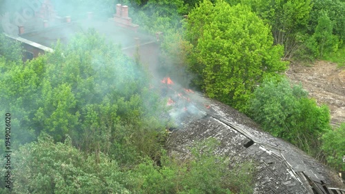 Flames burst through the roof of a one-story building while thick smoke rises into the sky.

