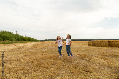 Children run on the mown wheat field where there are sheaves.