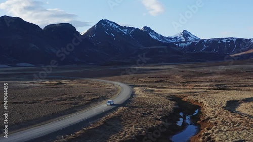 White van driving on a lonely road between snowy mountains in Iceland