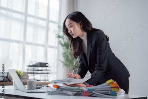 Fotografie Young Asian businesswoman managing a large pile of documents and files on her de