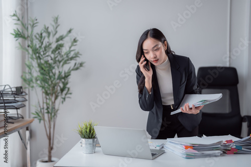 Fotografi Asian businesswoman managing multiple tasks, talking on a mobile phone while han