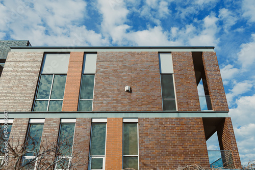 Brick building stands under a cloudy sky in an urban area during the daytime while showcasing modern architectural design elements and large windows