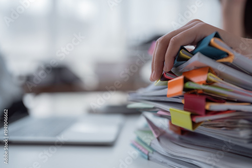 Employee hand grasping a tall pile of folders and papers fastened with colorful binder clips, symbolizing office workload, administrative burdens, and the task of organizing records