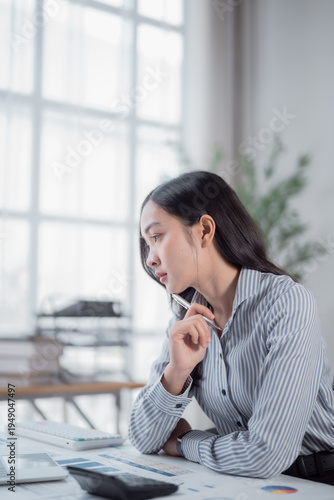 Obraz na plátně Young Asian business woman sitting at a modern office desk, concentrating and ho