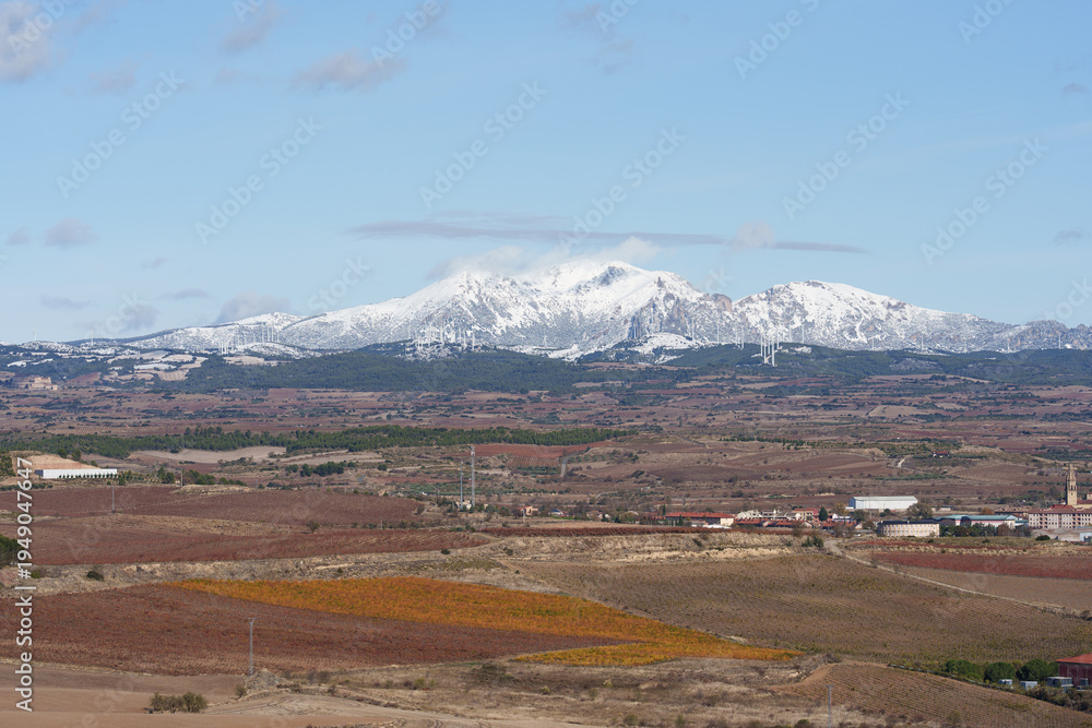 Naklejka premium Snowy Mountain Range Overlooking Autumn Vineyards and Village
