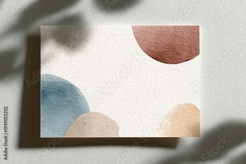 Abstract watercolor painting of rounded shapes on textured paper with leaf shadow
