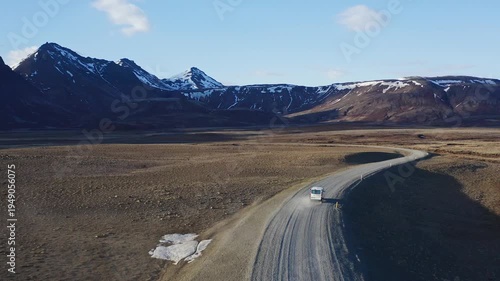White van driving on a lonely road between snowy mountains in Iceland