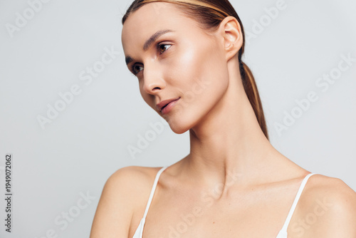 Obraz na plátně A close-up portrait of a young woman with flawless skin and minimal makeup looks thoughtfully to the side against a neutral grey background