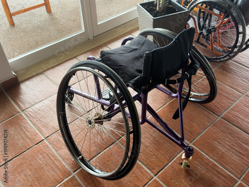 Foto Lightweight wheelchair featuring a purple padded seat, foldable design for easy storage, and durable silver frame with adjustable footrests for user comfort and mobility