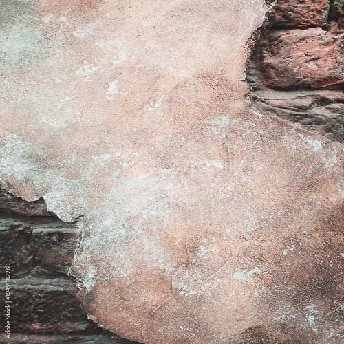 Weathered stone surface shows signs of age and erosion. Soft pink tones contrast with darker, rough textures. Cracked and flaking areas reveal layered history
