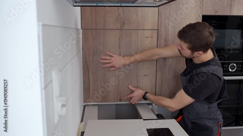 Man in overalls installing wooden kitchen cabinet door in modern apartment interior. Concept of home renovation self made furniture assembly and repair service