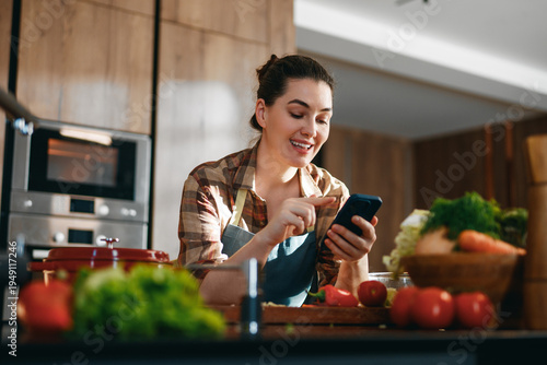 Smiling Woman Cooking and Using Smartphone in Modern Kitchen