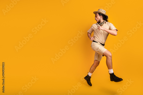 Schilderij op canvas Man in safari outfit leaps against bright yellow backdrop evoking adventure trav