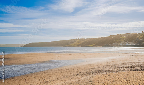 Canvas Print A sandy beach with clouds above and a headland in the distance.