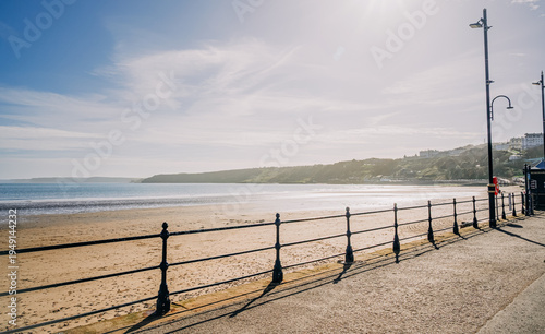 A sandy beach with a headland in the distance and a promenade in the foreground.