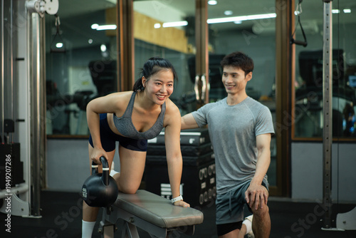 Konstfotografi A woman is performing a kettlebell row on a bench while her trainer closely chec