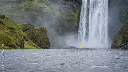 Wide shot of huge waterfall and river with people walking around, Iceland