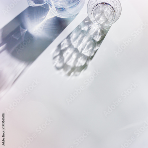 Water Glass with shadows at sunlight on white, delicate green blue color, minimal aesthetic top view shiny glasses at natural light, summer drink concept, pastel gradient interplay light and shadow