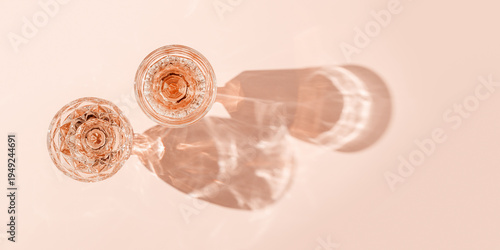 Top view two glasses of rose wine on peach color background, beautiful shadow at sun. Vintage wineglass minimal life style, close up sparkling alcohol drink, summer holiday mood, festive banner