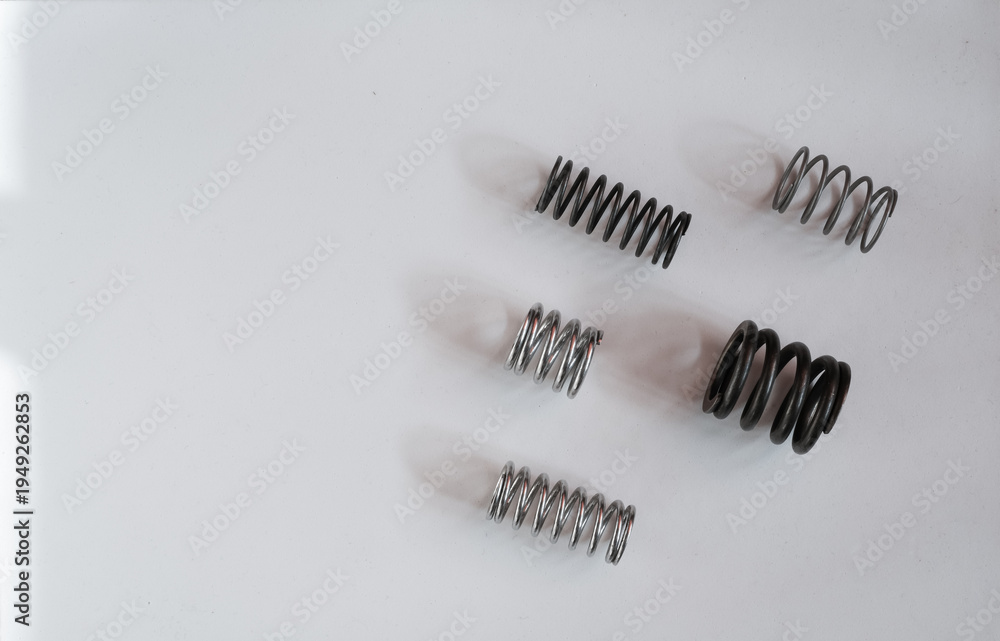 Fototapeta premium Set of metal coil springs on a white surface. Engineering, mechanics, industrial components. Top view. Copy space.