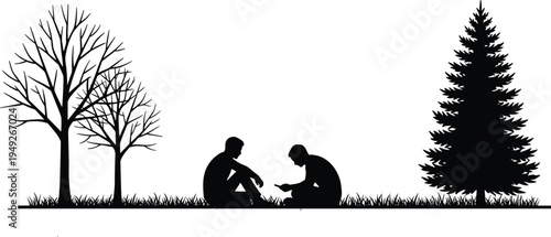 Black silhouette of two young men sitting on grass between a pine tree and leafless trees while using a smartphone in a park.