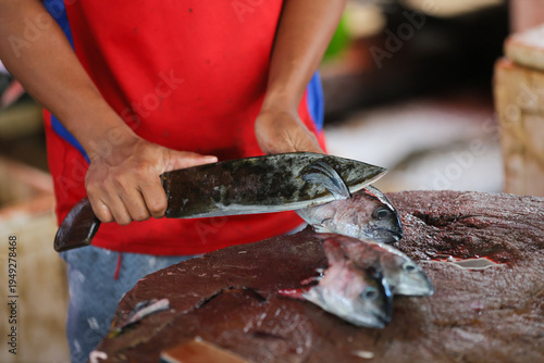 Detailed view of a vendor chopping fresh fish into smaller pieces at a busy local seafood market
