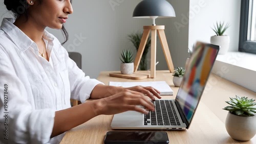 Focused Young Woman Working on Laptop and Checking Smartphone in Minimalist Home Office