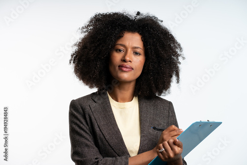 Photo of gorgeous black secretary woman with afro hairstyle writing down notes in clipboard while working in office