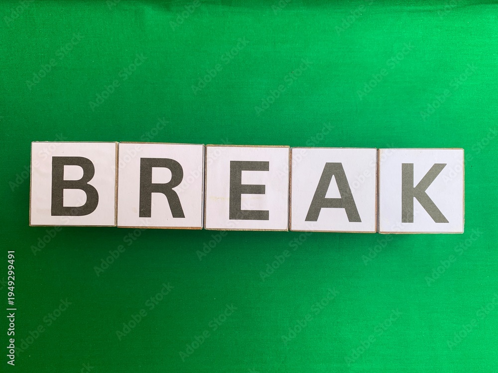 Obraz premium The word BREAK spelled out with white alphabet letter tiles on a solid bright green fabric background. Flat lay concept.