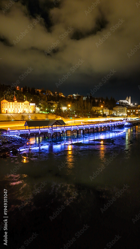 Fototapeta premium Drone view of Akureyri in North Iceland at night with illuminated bridge and city lights reflecting on water. Beautiful aerial scene of Akureyri harbor showing urban landscape and coastline in Iceland