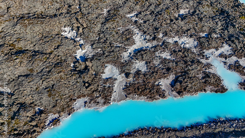 Drone view of the Blue Lagoon in Iceland with bright blue geothermal water surrounded by dark lava fields. Famous Iceland spa with steam, volcanic landscape, and tourists bathing in warm lagoon.