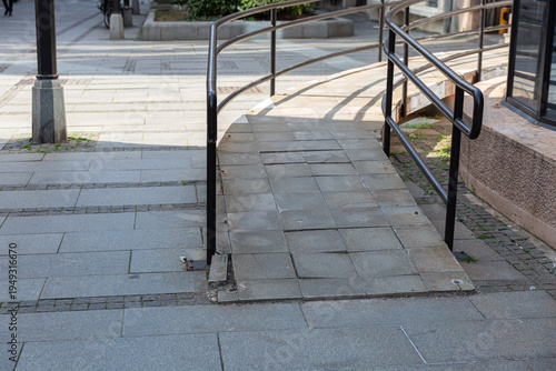 Wallpaper Mural Metal Railing Guides Concrete Accessibility Ramp And Sidewalk, Daylight Casting Crisp Shadows Over Tiles And Curb, Urban Planning Detail Focused On Safe Pedestrian Flow, Inclusive Design, Mobility Torontodigital.ca