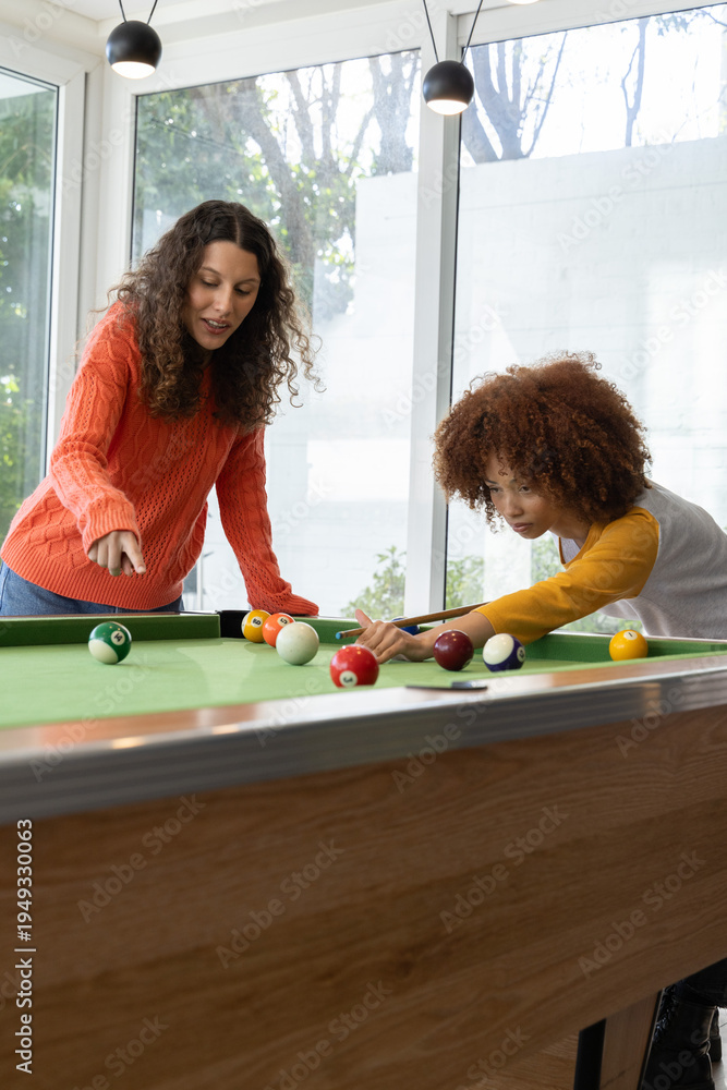 Fototapeta premium Diverse female friends playing pool in bright game room with green felt table cues scattered balls