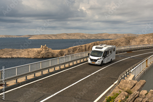 Obraz na płótnie A high-angle scenic shot of a modern white camper van (RV) driving across the famous Pag Bridge (Paski most) in Croatia