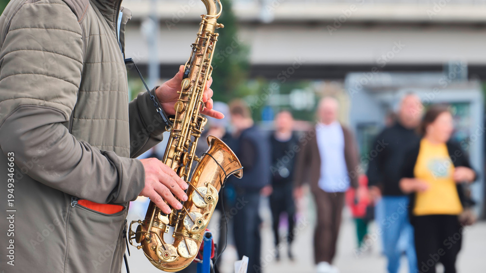 Fototapeta premium Street musician performing jazz music with a saxophone for passersby on a city sidewalk.