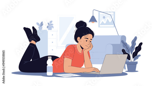 Young woman lying on the floor with her legs up while working on a laptop computer in her cozy home office at home.