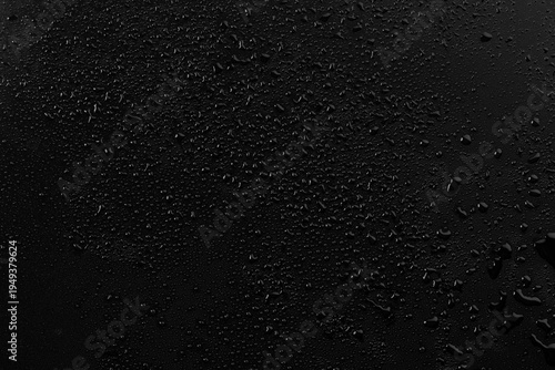 Water droplets on a black surface create patterns that catch light and shadows