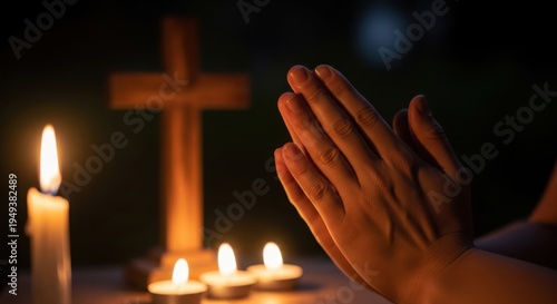 Hands in prayer position with wooden cross and candles in dark background