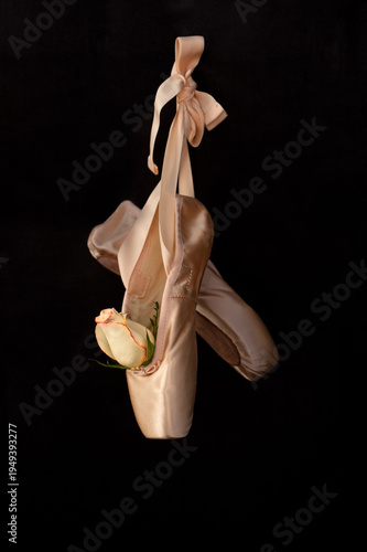 ballet slippers with rose hanging on black background