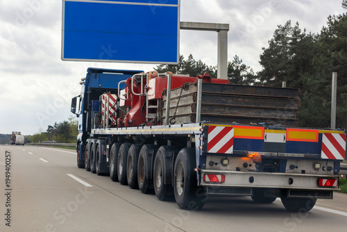 Fotografia Heavy flatbed truck transporting industrial machinery crane counterweight highway road cloudy sky commercial freight transport