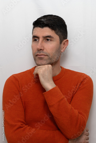 Wallpaper Mural Studio portrait of a man in an orange sweater, posing with his fist or hand under his chin. He is looking off-camera with a calm, serious, and thoughtful expression. Torontodigital.ca