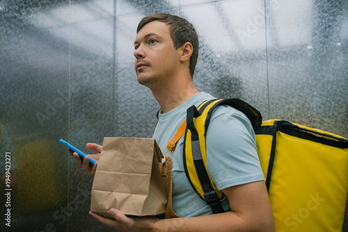 Photography Delivery man carrying a paper bag and a large yellow insulated backpack, using a