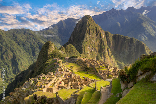 Panoramic view of Machu Picchu Inca citadel with Huayna Picchu mountain in the background under a blue sky. Ancient stone ruins and agricultural terraces in the Andes Mountains of Peru.
