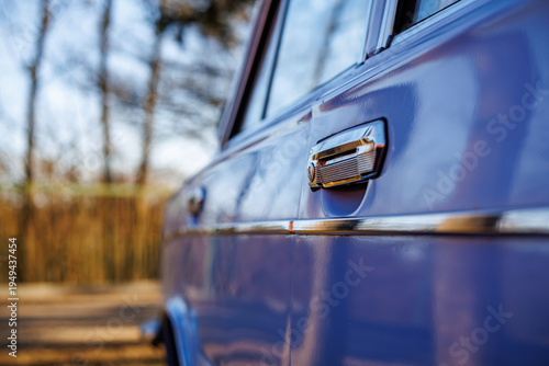 Tablou pe pânză Close-up of a blue vintage car front: headlights, chrome grille and retro whitewall tires on a cobblestone road