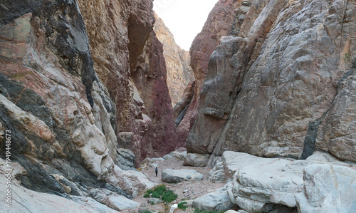Dramatic landscape of a deep narrow canyon in lower Wadi Isla, Saint Katherine Protectorate in Egypt. High cliffs and steep granite walls. Red, green, black colors of magmatic rock. A female tourist.