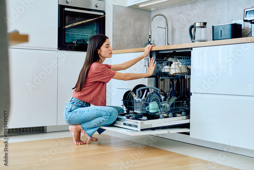 Canvastavla Woman loading dirty dishes into a modern dishwasher appliance, performing a dail